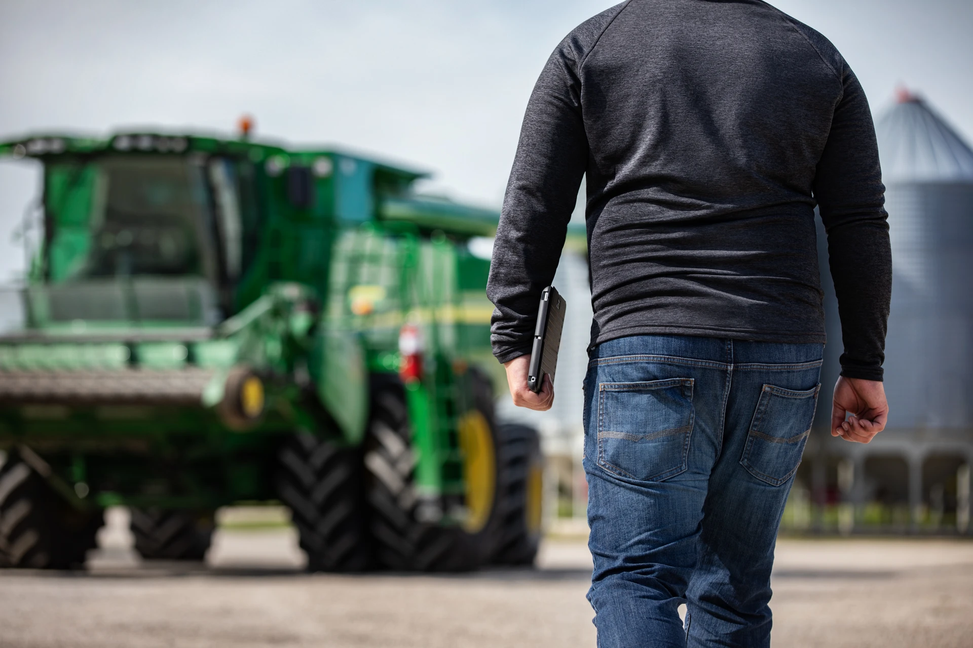 Agronomist walking towards farm implements carrying a tablet. 