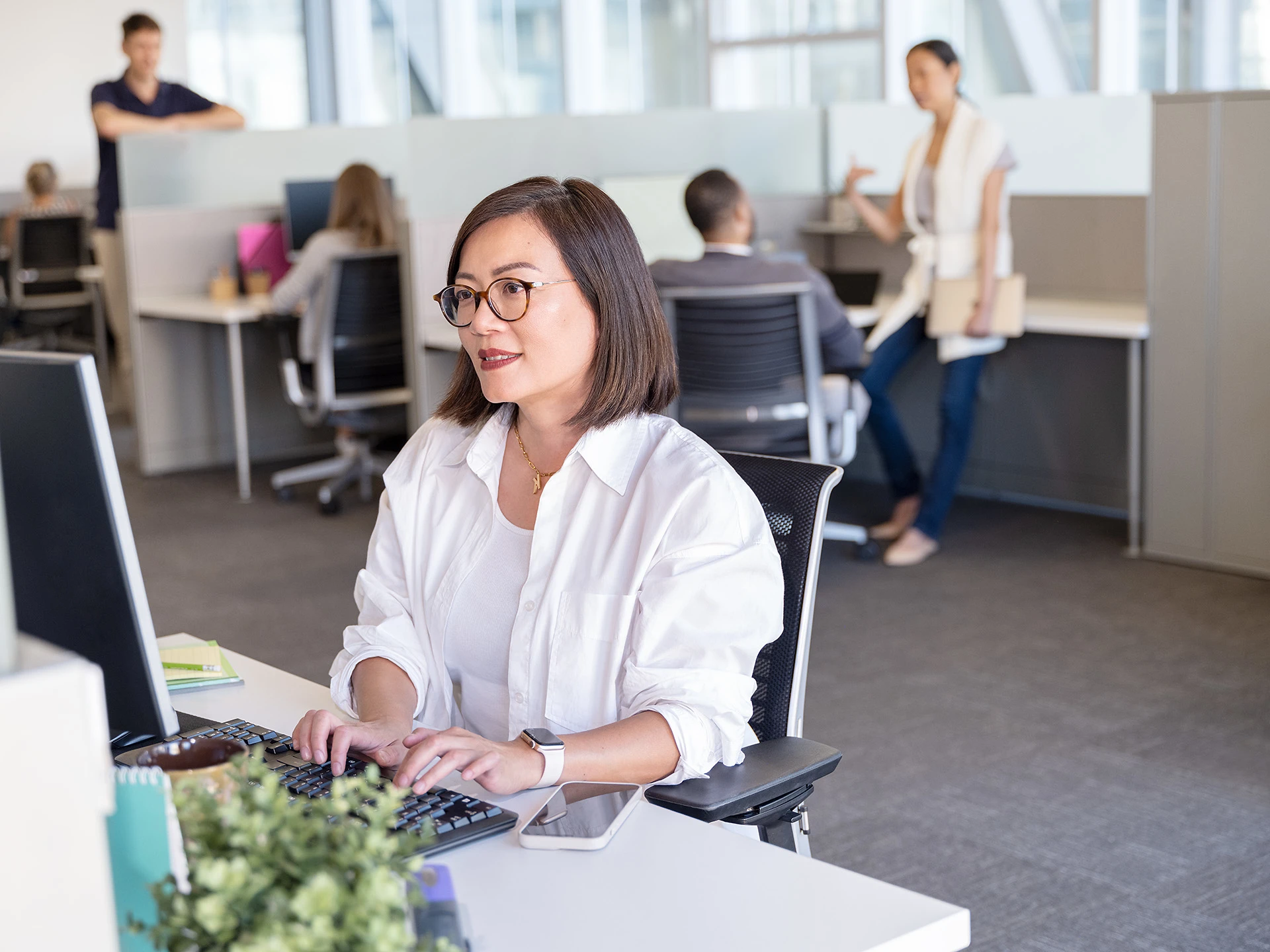 A woman wearing glasses sits at a desk in an office, focused on rebate management in the agriculture sector.