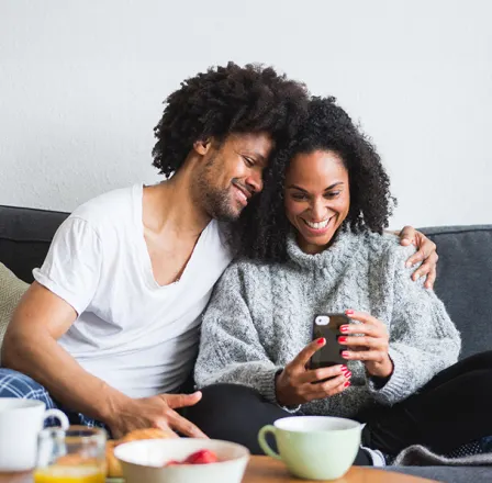 A couple are seen on the couch reviewing cameras on the TELUS SmartHome+ app.