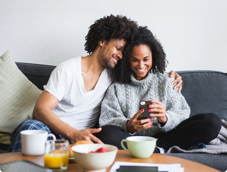 A couple are seen on the couch reviewing cameras on the TELUS SmartHome+ app.