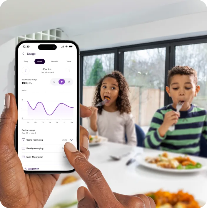 A hand holds the TELUS SmartHome+ app while the kids are eating breakfast showing energy usage and trends over time. 