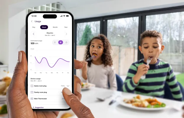 A hand holds the TELUS SmartHome+ app while the kids are eating breakfast showing energy usage and trends over time. 