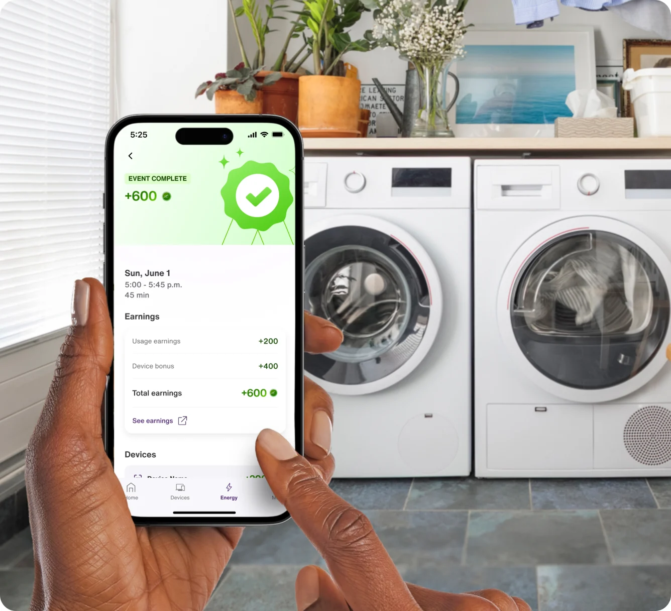 A hand holds the TELUS SmartHome+ app while doing the laundry and seeing a summary of a successful energy savings event completed. 