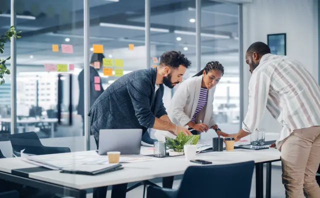 Three colleagues, leaning over a table while working 