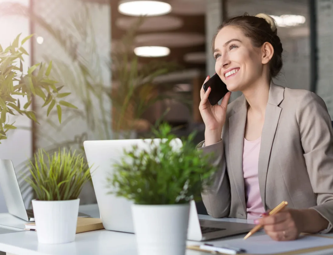 A smiling woman on the phone working at her desk