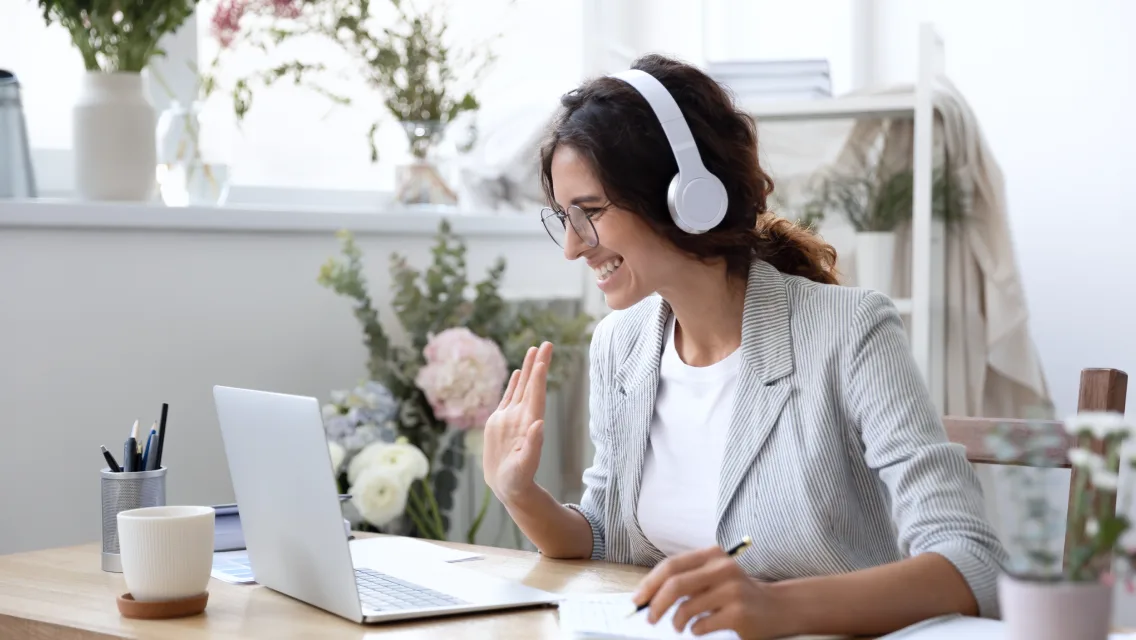 A girl with headphones waving at the laptop screen