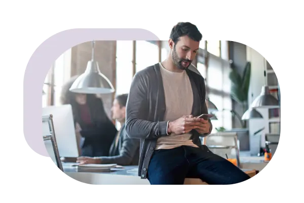 A person using their smartphone, casually sitting on a desk in a modern industrial-style office.