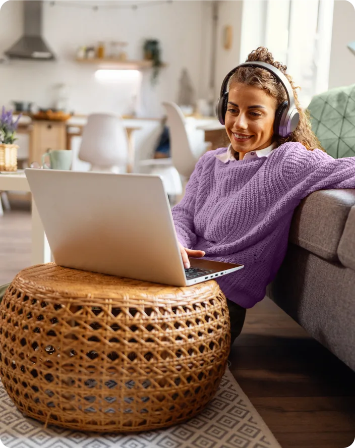 An image of a young woman sitting on the floor of her living room, reading the TELUS SmartEnergy blog on her laptop. She is dressed in relaxed clothing and she has a calm and happy facial expression.