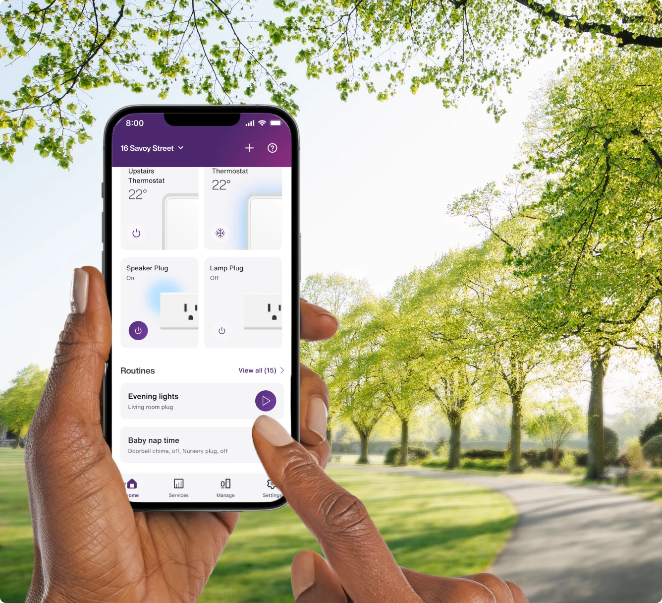 A hand holds the TELUS SmartHome+ app while out on a walk in the park showing the control of thermostats, smartplugs and routines.